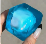 Squishy cube bleu translucide rempli de petites gommes tenu dans une main