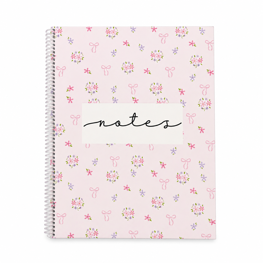 Cahier de notes rose pâle à spirale avec motifs de fleurs et nœuds sur fond blanc