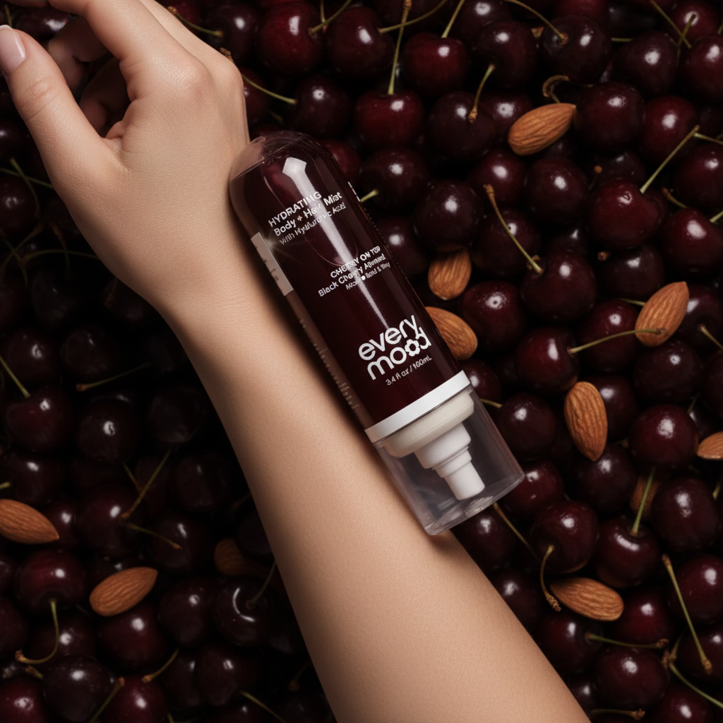 Main tenant la brume Every Mood Cherry On Top contre la peau, cerises noires et amandes en arrière-plan, ambiance bold et sensuelle