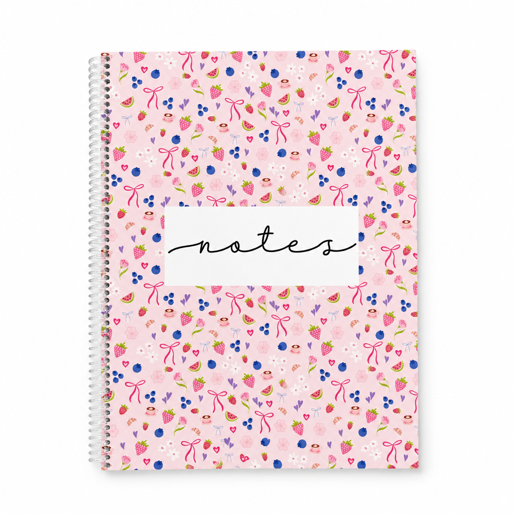 Cahier de notes à spirale rose avec motifs de fruits et rubans sur fond blanc